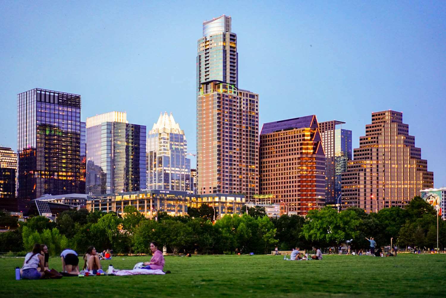 A view of the Austin, Texas skyline from a park with green grass & people..